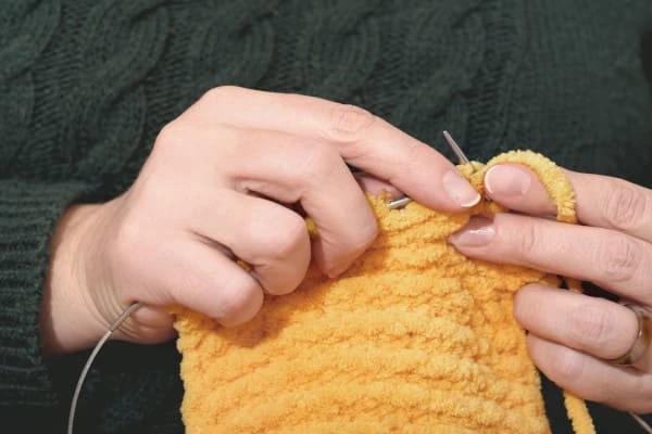 Mãos de mulher tricotando lenço amarelo com agulhas acessórios feitos à mão vestuário de malha